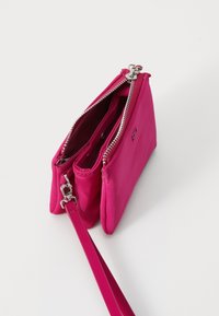 Pink crossbody bag made of smooth material, featuring two zip compartments, silver-tone hardware, and a detachable strap.