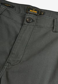 Schmal geschnittene, dunkelgraue Hose aus strapazierfähigem Stoff, mit einem vorderen Knopfverschluss und einem Markenlabel am Bund.