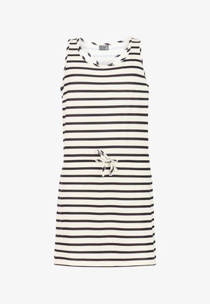 Meisje met lang bruin haar, gekleed in een mouwloze zwart-wit gestreepte jurk en zwarte slippers, staand met één hand op haar heup.