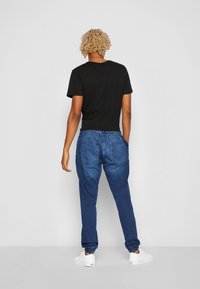 Camiseta negra de manga corta combinada con pantalones jogger de denim azul con puños elásticos y bolsillos traseros, vista desde atrás.