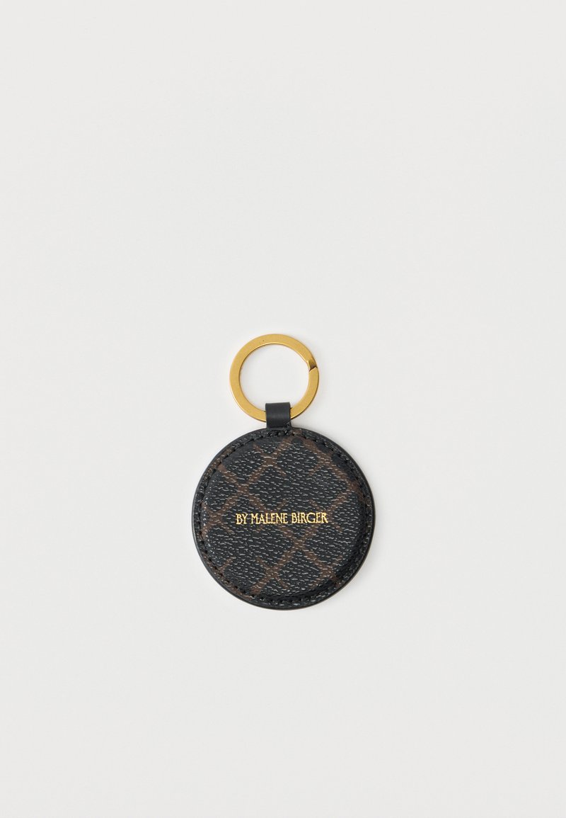 Στρογγυλό μαύρο δερμάτινο μπρελόκ με καφέ γεωμετρικό μοτίβο, χρυσό κρίκο και χρυσό κείμενο "BY MALENE BIRGER" στο κέντρο, σε λευκό φόντο.