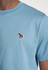 Jasnoniebieska bawełniana koszulka z krótkim rękawem, z małym wielokolorowym haftowanym zebrem na lewej piersi oraz okrągłym dekoltem.