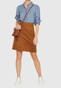 Camicia di jeans con colletto arricciato, gonna in suede marrone e sneakers bianche. Piccola borsa marrone con tracolla.