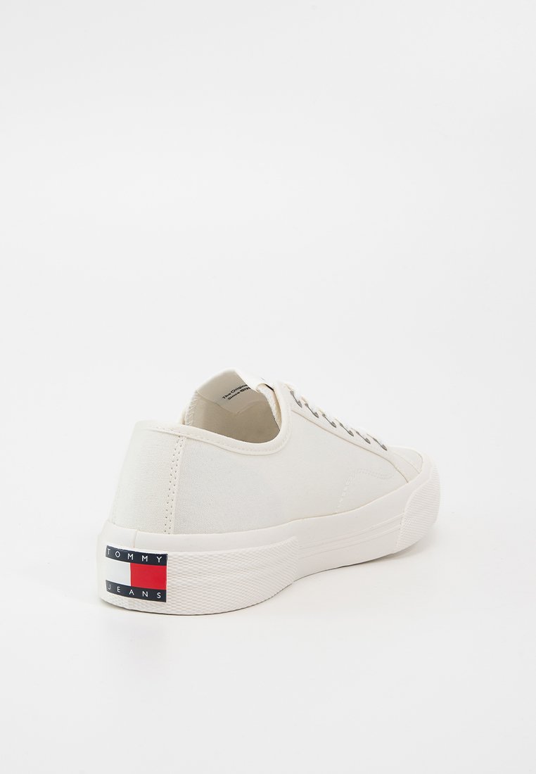 Zapatillas de lona blancas con diseño de caña baja, punta redonda y suela de goma texturizada. Presenta una etiqueta de acento de color en el talón.