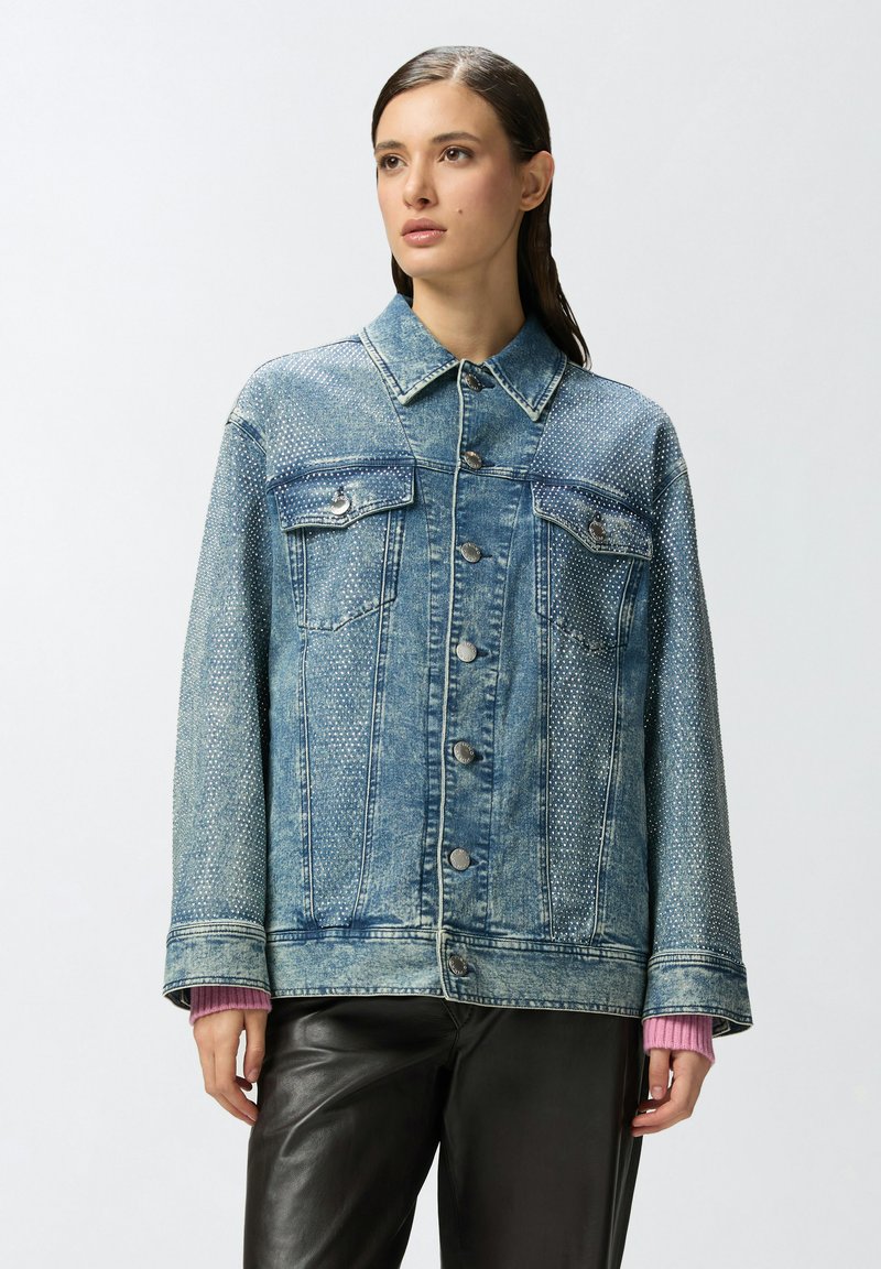 Traper jakna u svijetloplavoj boji s kopčanjem na gumbe, dva džepa na prsima i dekorativnim teksturiranim detaljima. Pretjerano širok kroj s manžetama.