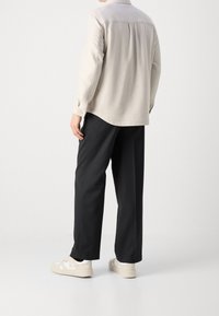 Camisa de manga larga gris claro con yugo trasero, combinada con pantalones negros de corte holgado y zapatillas beige. Textura plana, diseño minimalista.