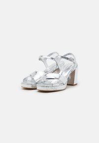 Sandali argento metallici con tacco a blocco chunky, design con fasce incrociate e finitura testurizzata. Punta aperta con cinturini alla caviglia.