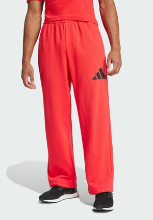 Røde, løst siddende sweatpants lavet af bomuld; en elastisk livrem og et sort Adidas-logo på venstre side. Struktureret, casual design.