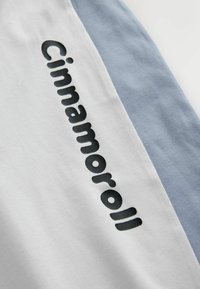 Biała bawełniana tkanina z jasnoniebieskim panelem. Odważny czarny napis "Cinnamoroll" biegnie pionowo wzdłuż białej sekcji. Gładka tekstura.