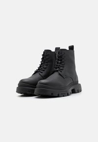 Bottes chelsea en cuir noir avec finition texturée, design à lacets, semelle en caoutchouc épaisse et accent de marque. Comprend une languette pour un enfilage facile.