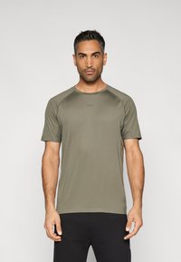 Oliwkowa zielona sportowa koszulka z krótkim rękawem, okrągłym dekoltem i raglanowymi rękawami. Na piersi subtelne logo, gładka faktura.