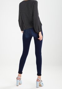 Blusa nera a pois con maniche a campana, abbinata a jeans aderenti blu navy e scarpe con tacco alto azzurre chiare con lacci.