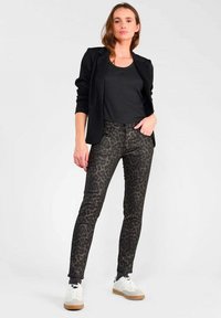 Svart kavaj över en svart topp, kombinerat med figurnära leopardmönstrade jeans i mörka toner. Modellen bär vita sneakers med bruna detaljer.