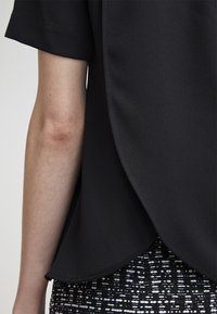 Blusa nera con orlo curvo e maniche corte, abbinata a una gonna a righe in bianco e nero con texture. Tessuto liscio e leggero.