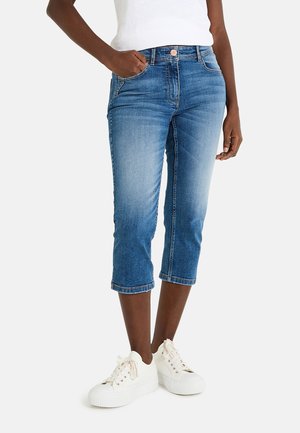 Pantalons capri en denim bleu moyen avec une finition délavée. Présente un design classique à cinq poches, un ourlet retroussé et des accents cousus.