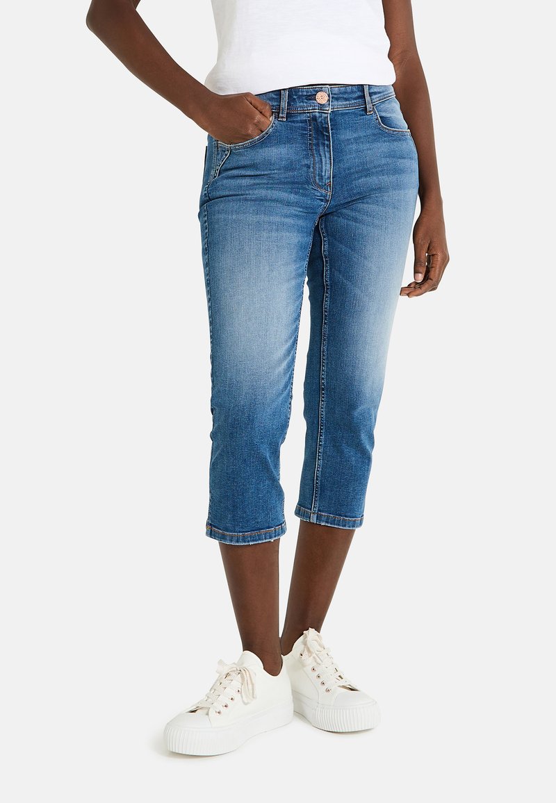 Pantalones capri de mezclilla en azul medio con un acabado desgastado. Presenta un diseño clásico de cinco bolsillos, dobladillo enrollado y acentos cosidos.