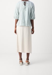 Vaaleansininen tekstuuriyläpaita lyhyillä puffihihnoilla, jossa on takana nauhakiinnitys, yhdistettynä kermankeltaiseen nilkkapituisen hameeseen ja beigeihin paksupohjaisiin sandaaleihin.