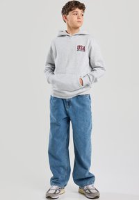 Gray hoodie with kangaroo pocket, featuring "USA NEW YORK CITY" in red text. Paired with loose-fitting blue jeans and gray sneakers.