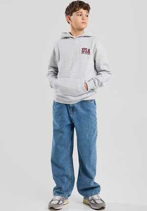 Felpa grigia con tasca a marsupio, con la scritta "USA NEW YORK CITY" in rosso. Abbinata a un paio di jeans blu a vestibilità ampia e scarpe da ginnastica grigie.