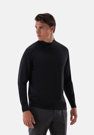 Black long-sleeve mock-neck sweater made of smooth fabric, featuring a fitted silhouette and minimal design, paired with gray trousers.