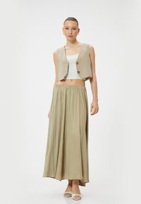 Chaleco corto beige con dos botones, combinado con una larga falda verde claro de cintura alta y fluida. Tela suave, diseño minimalista.