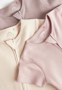 Three short-sleeved tops in soft ribbed fabric: one light beige, one soft pink, and one deeper mauve, featuring a front snap closure.