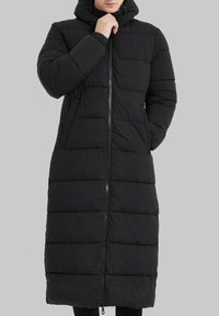 Manteau long noir rembourré avec capuche, fermeture éclair à l'avant et poches latérales. Design de type doudoune texturé avec des sections matelassées horizontales.