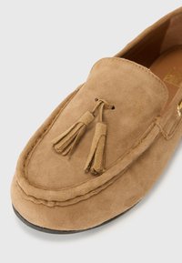 Semišové loafers v svetlo hnedej farbe s zaoblenou špičkou, doplnené strapcami a viditeľným šitím pozdĺž okrajov. Hladká vnútorná podšívka.