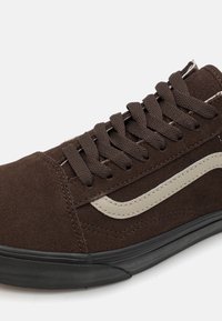 Baskets montantes en daim marron avec des lacets plats foncés et une bande latérale couleur crème. Elles présentent une semelle extérieure en caoutchouc noir texturé pour une meilleure adhérence.