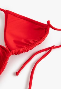 Punainen bikinitoppi joustavasta kankaasta, jossa on kolmiomaiset kupit, rypytetty reunus ja säädettävät siteet mukautettavan istuvuuden saavuttamiseksi.