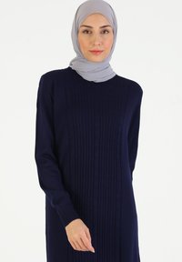 Abito lungo lavorato a maglia blu navy con motivo verticale testurizzato, scollatura tonda e maniche lunghe. Accompagnato da un hijab grigio chiaro.
