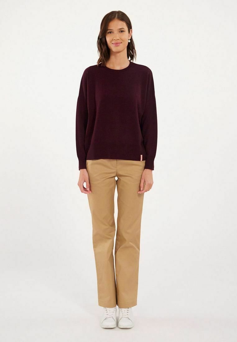 Pull bordeaux à manches longues, coupe décontractée ; associé à un chino beige et des baskets blanches. Design simple, sans motifs ni éléments métalliques visibles.
