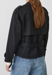 Zwarte trenchcoat met een cropped ontwerp, dubbelzijdige knopen en een ceintuur in de taille. Heeft lange mouwen en een gelaagde achterkant.