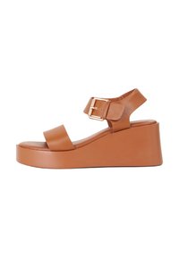Sandalo con zeppa in pelle color tan, con una larga fascia sulla punta, cinturino alla caviglia regolabile con fibbia dorata e una suola piatta liscia e arrotondata.