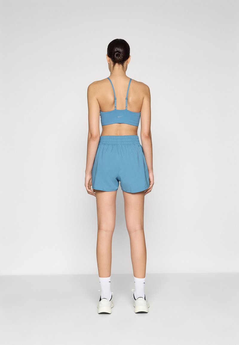 Conjunto deportivo de color azul claro que incluye un sujetador deportivo ajustado y pantalones cortos holgados. La tela tiene una textura suave, con tirantes finos y una cinturilla elástica.