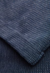 Close-up van donkerblauw gestructureerd stof met fijn geweven patroon en een gevouwen rand.