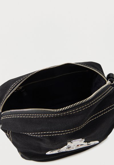 Fekete szövettáska fehér varrással és ezüst cipzárral, részben nyitva, üres belső térrel, az elején ezüst fém jelvénnyel.