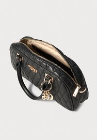 Black quilted handbag with gold hardware, top zipper, dual handles, and a branded decorative charm; features a light beige interior lining.