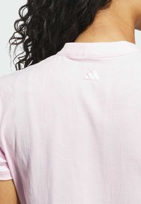 Lyst rosa sportstrøje med et struktureret mønster og et lille broderet logo på bagsiden af nakken. Kortærmet med rund halsudskæring.