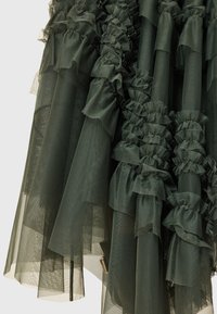 Falda de tul en un verde oscuro, con capas que presentan volantes a lo largo de las costuras. La tela es ligera y cuenta con diferentes texturas y longitudes de dobladillo.