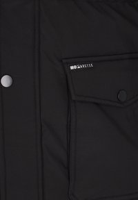 Tissu de veste noir avec une poche rectangulaire cousue présentant un rabat et un bouton-pression noir, ainsi qu'une petite étiquette mentionnant « MOMARCTIC ».