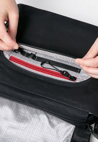 Borsa nera con zip e interno a motivo a rete grigia. Presenta più tasche, tra cui un compartimento rosso con zip e accessori metallici neri.