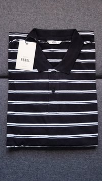 Camisa polo às riscas horizontais em preto e branco com colarinho preto, dois botões e uma etiqueta pendurada com a inscrição "REBEL" sobre um fundo de tecido cinza.