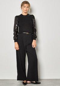 Czarny zestaw składający się z dopasowanej czarnej sweterka z rękawami w kształcie puff, oraz czarnych spodni z wysokim stanem i szerokimi nogawkami, dopełniony czarnymi balerinami.
