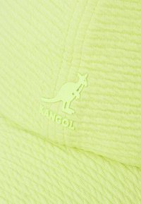 Căciulă Kangol de culoare galben neon, fabricată dintr-un material texturat, dotată cu un logo de cangur și detalii de cusătură vizibile pe margine și pe vârful căciulii.
