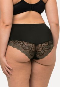 Zwarte panties met kantafwerking, voorzien van een gladde bovenband en ingewikkelde kantdetails langs de onderrand, die een semi-doorzichtige textuur benadrukken.