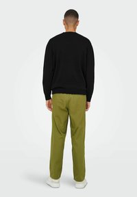 Black knit sweater with ribbed cuffs and hem paired with olive green trousers. Sneakers are white, set against a neutral background.