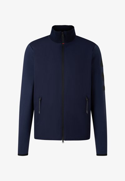 Granatowa kurtka zapinana na zamek z wysokim kołnierzem, przednimi kieszeniami na zamek oraz teksturowanym materiałem na kołnierzu i mankietach. Posiada subtelne akcenty logo na rękawie.