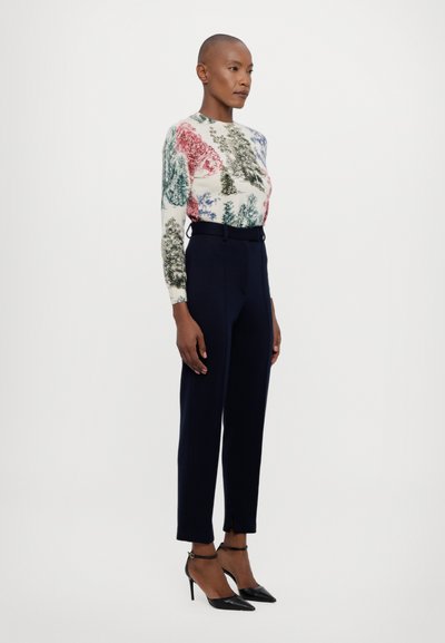 Knit sweater with multicolored tree prints; paired with fitted navy trousers with side slits; model wearing black pointed heels.
