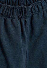 Pantaloni con elastico in vita di colore blu navy, realizzati in un tessuto di cotone texture. Presentano pieghe profonde e lati arricciati che migliorano comfort e vestibilità.